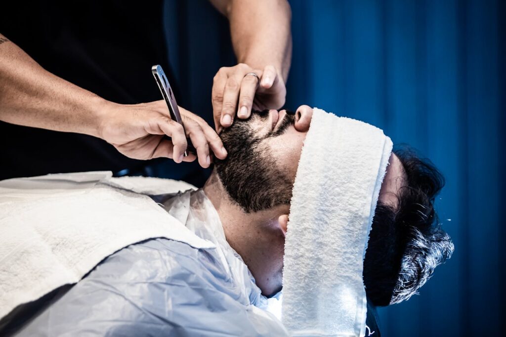 pexels-photo-6007400 An adult man receiving a precise beard trim in a barbershop with a warm towel treatment.