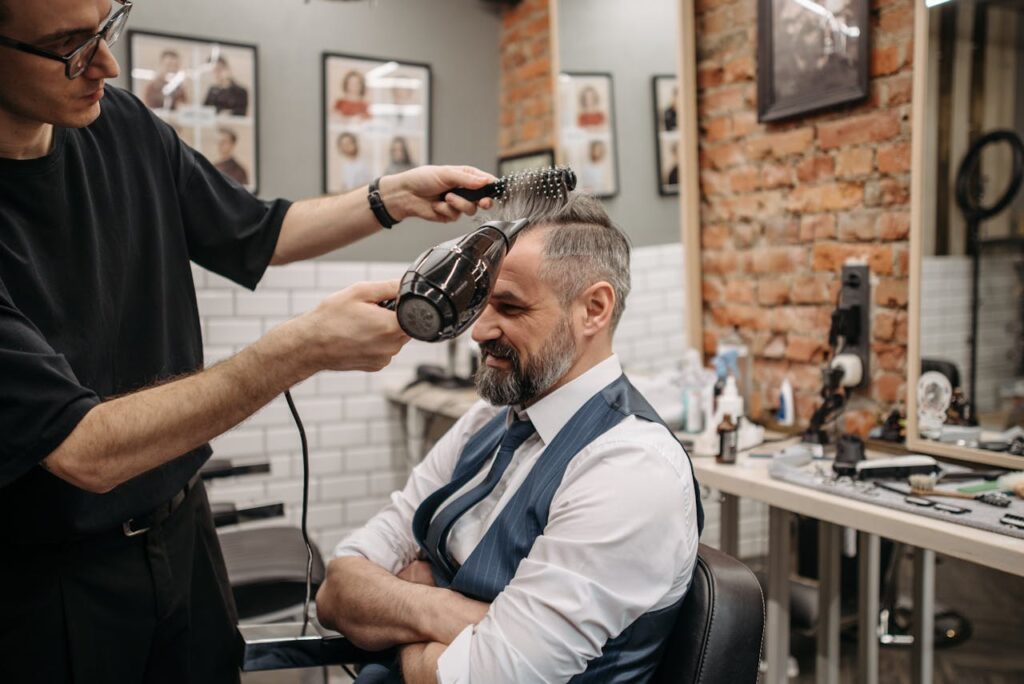 pexels-photo-7518761 An elderly man gets his hair blow-dried by a barber in a modern barbershop setting.