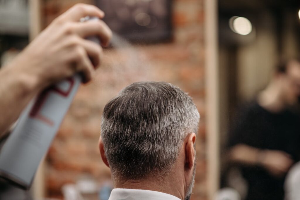 pexels-photo-7518763 A professional barber styles a man's hair with hairspray in an urban barbershop.